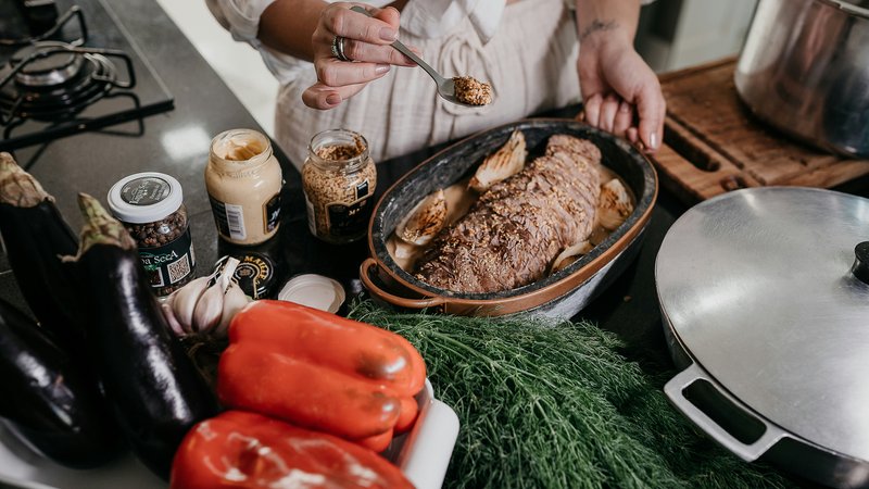 Vlees op smaak brengen met kruiden in een ovenschaal, omringd door verse groenten, als voorbereiding op een langzaam gegaard gerecht